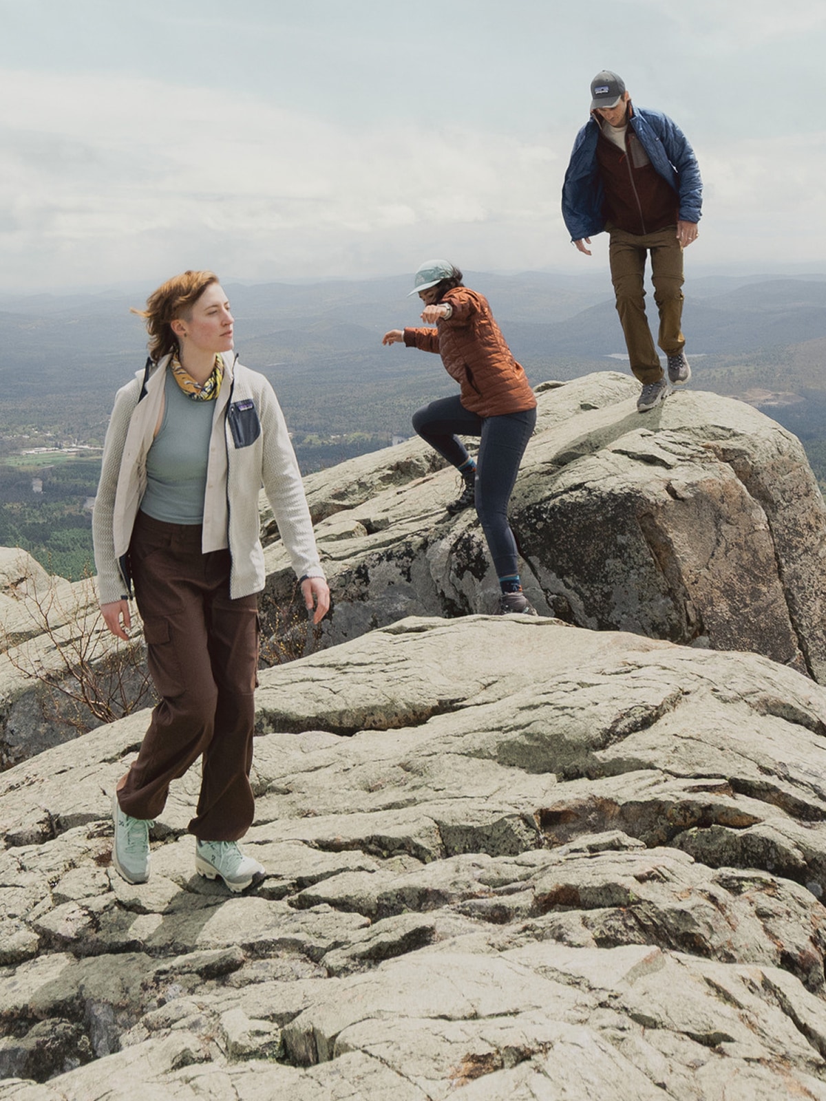 Three people hike across large rocks.