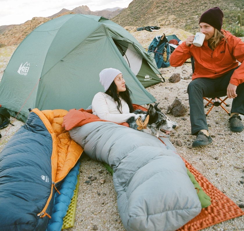 Two people and a dog spend time outside of their tent.