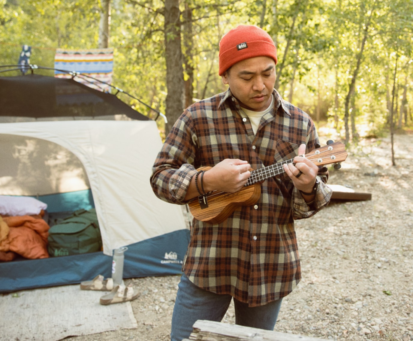 A person plays a ukulele at their campsite.