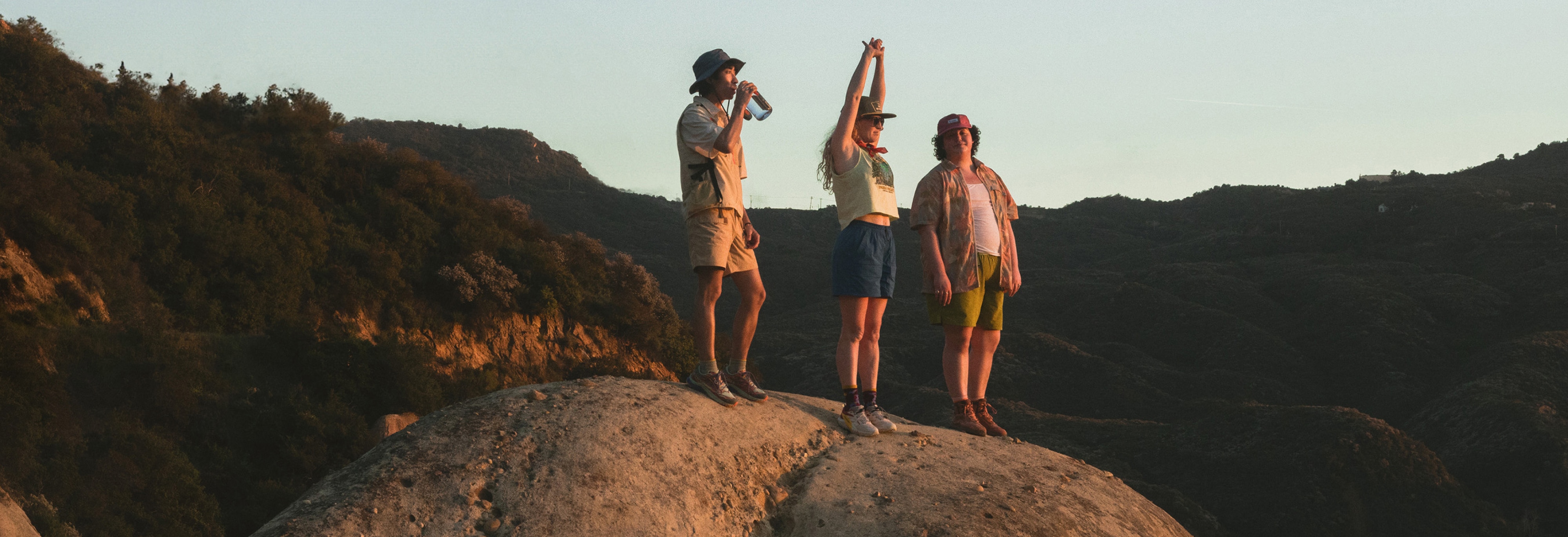A group of people stand on top of a large rock with grassy hills in the background.