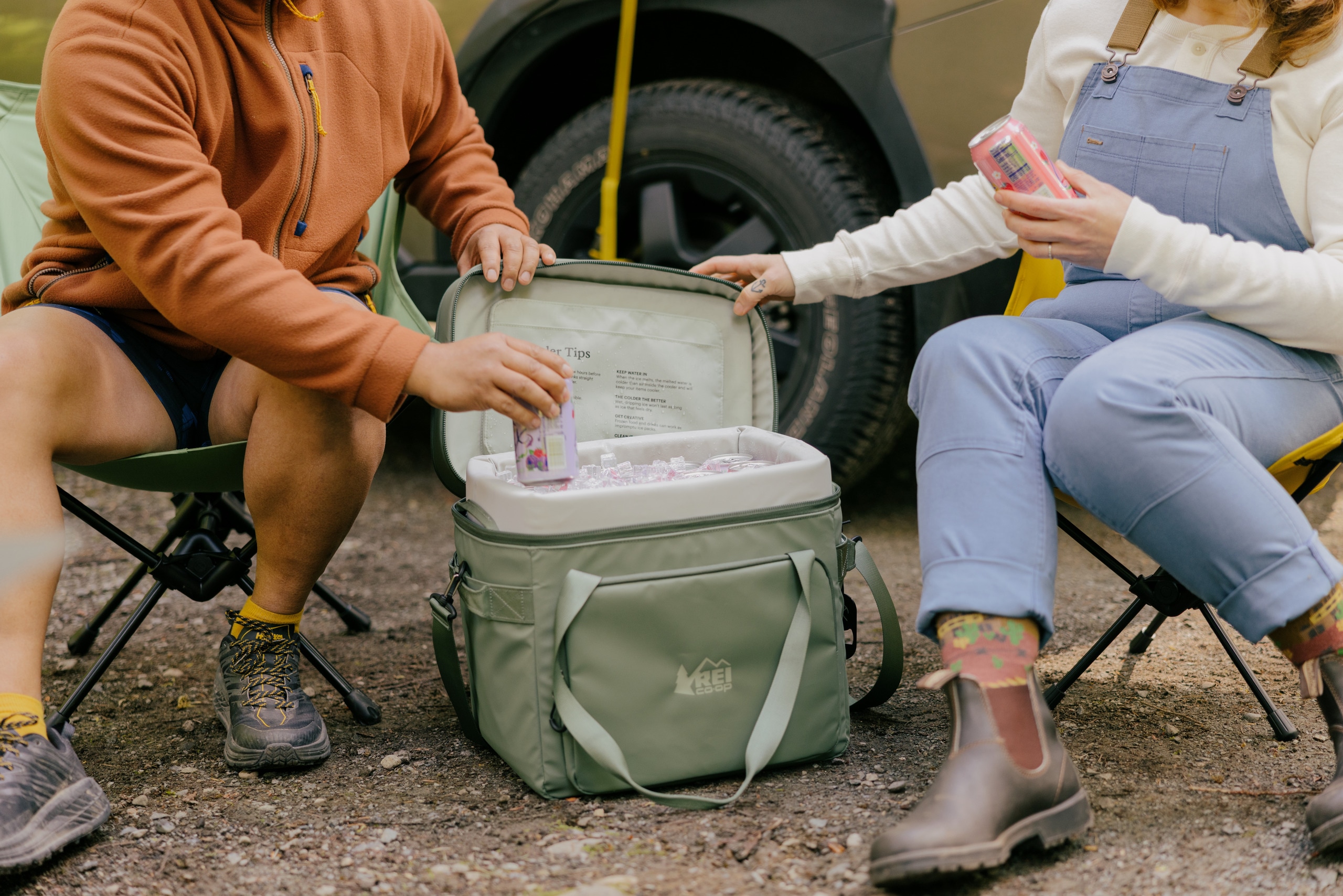 A green cooler sits between two adults who are hanging out at camp.