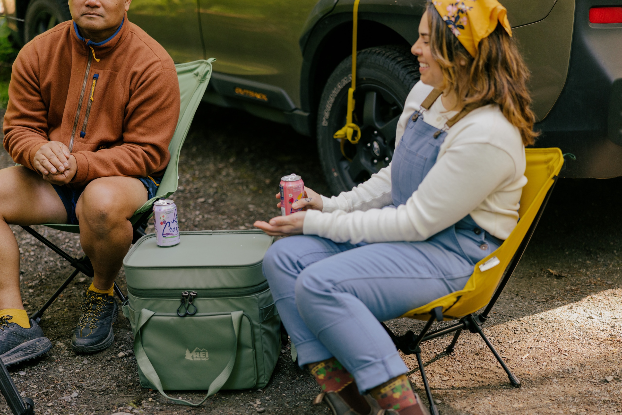 A picture of two people drinking sparkling waters while sitting in camp chairs.