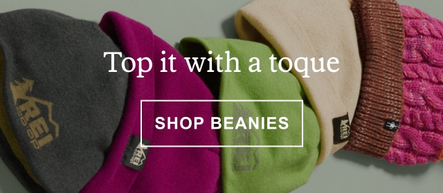 A studio shot of a varied assortment of beanies. Headline: Top it with a toque. Click to SHOP BEANIES