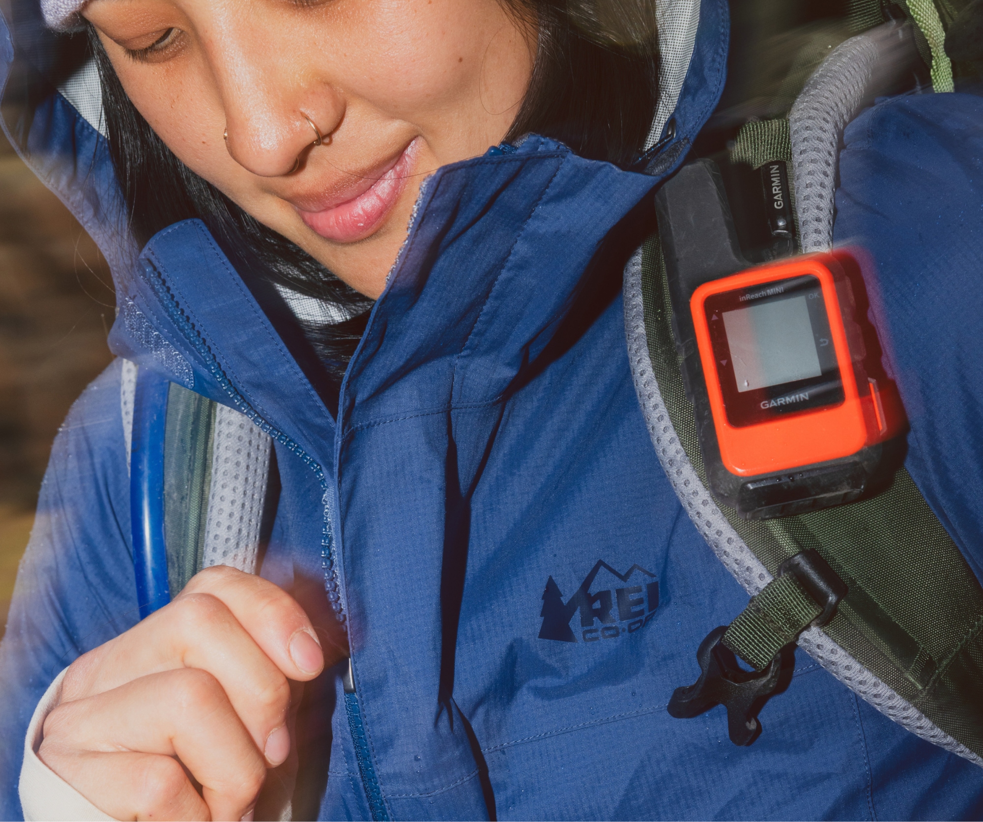 A person wearing an R E I Co-op brand jacket and a backpack with a Garmin inReach device.