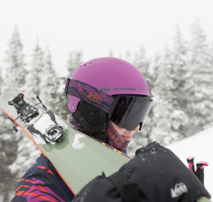 A person wearing a pink ski helmet while carrying skis.