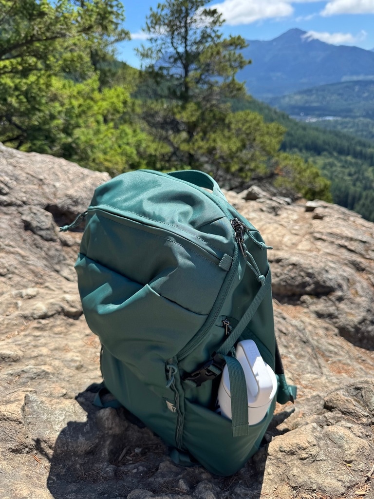 Photo of an REI Ruckpack on a rocky trail. A white water bottle is stashed in one of its side pockets.