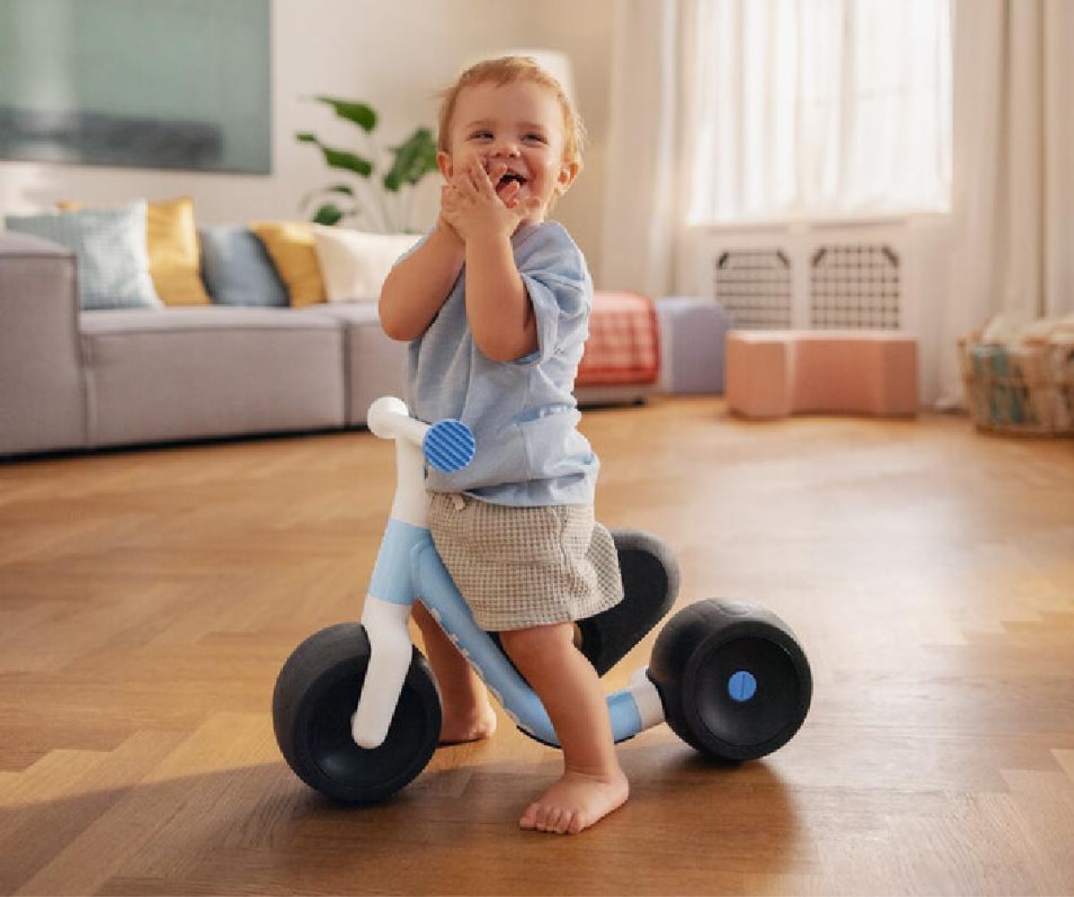 A child laughs and smiles for the camera while standing with their woom bike.