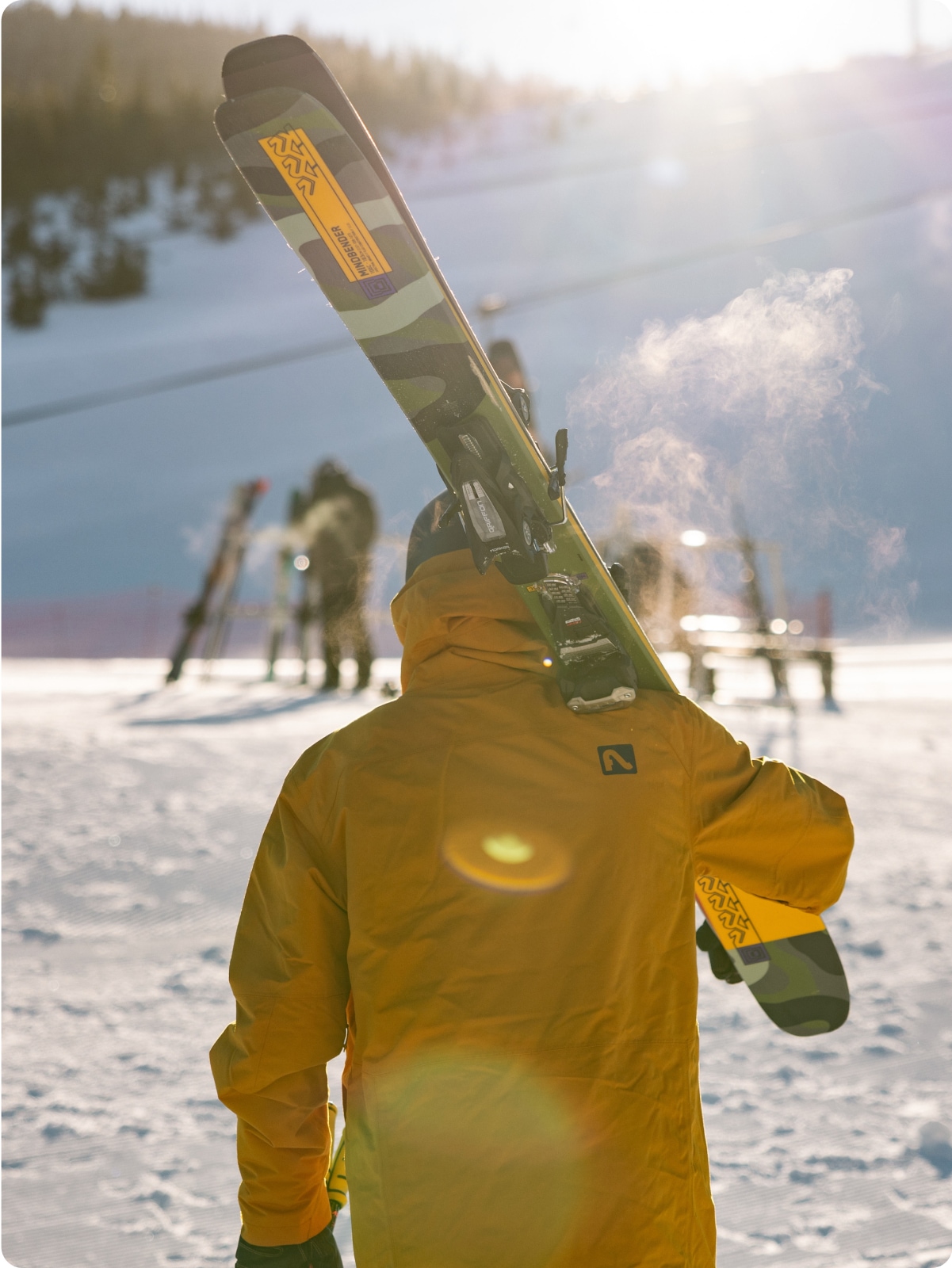A person faces away from the camera while carrying a set of skis.