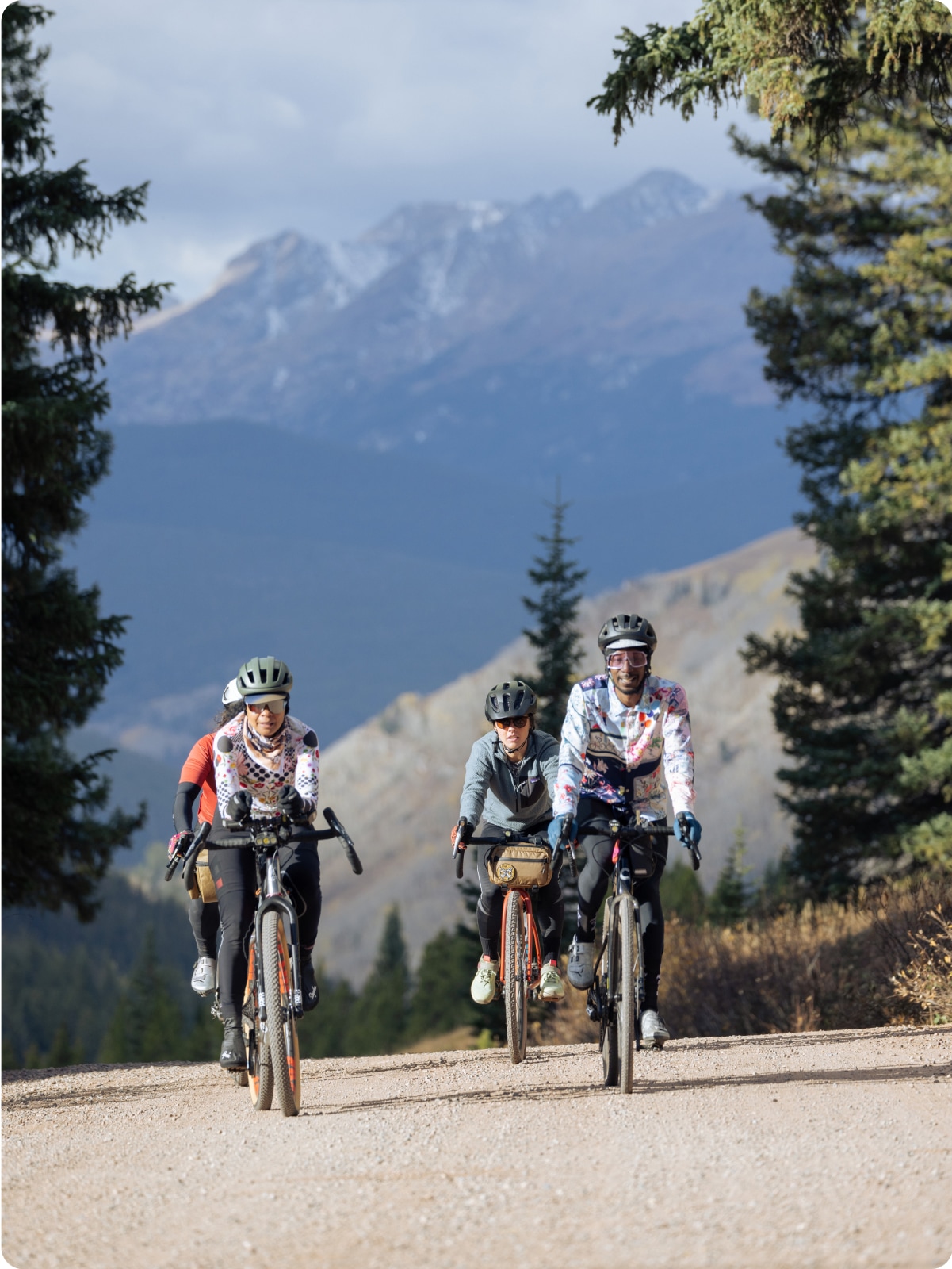 A group of people ride their bikes along a gravel road with a mountain range in the background.