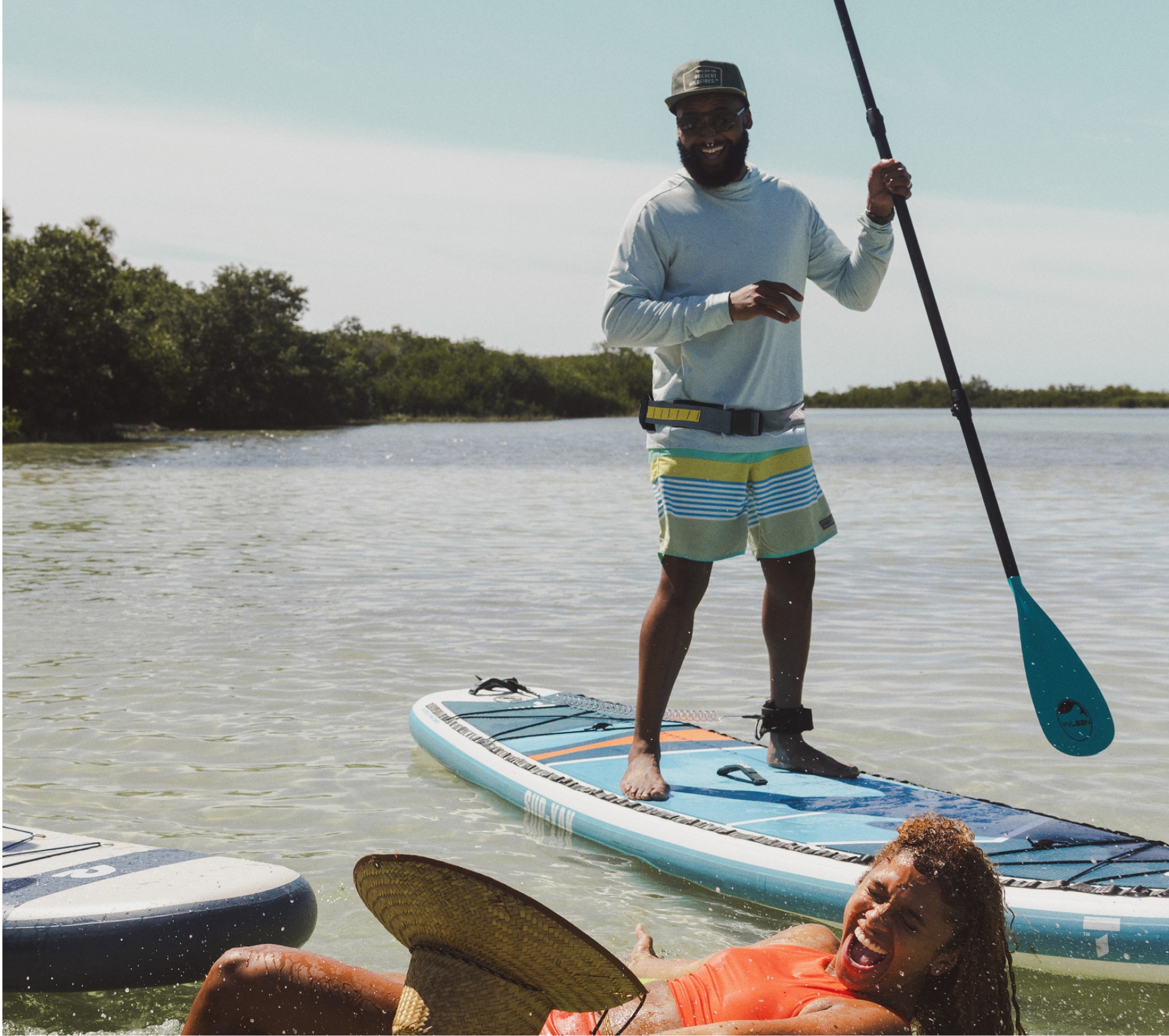 A person laughs while standing up on a paddleboard.