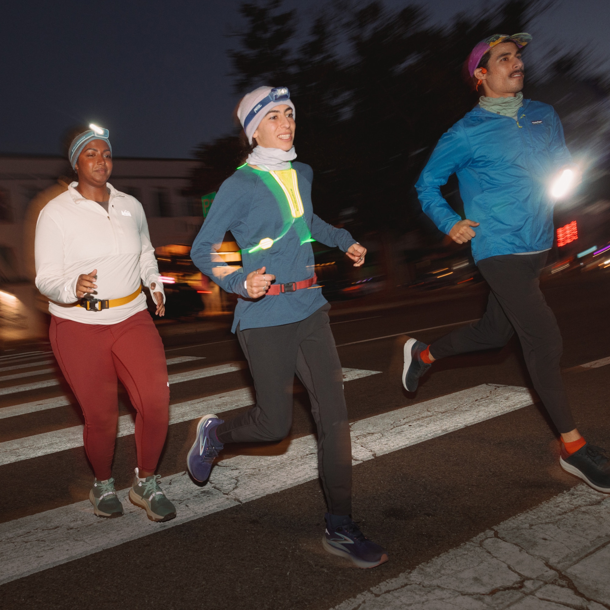 Three people dressed in winter clothing run across a crosswalk at night.