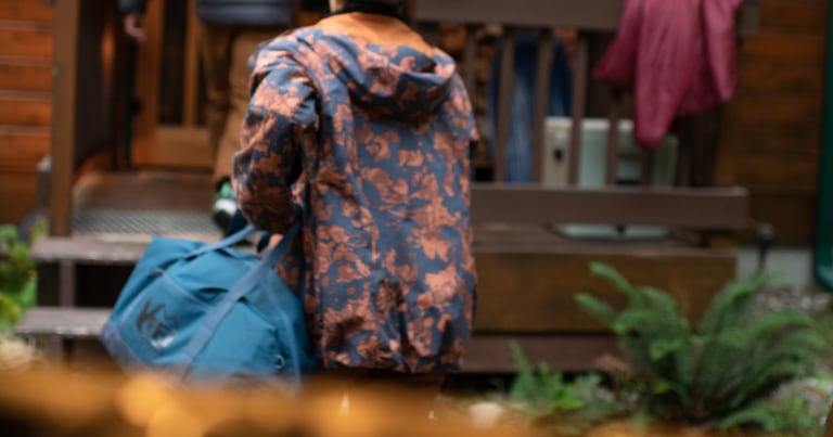 A person carries a blue duffel toward a lodge