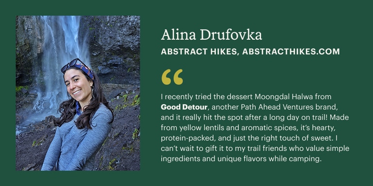 A person smiles standing in front of a waterfall. To her right is text that reads her name, Alina Drufovka and her brand is Abstract Hikes. She is recommending giving a gift from Good Detour, an outdoor snack company.