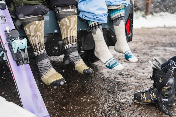 Two people sitting in their trunk after removing snowboots. 