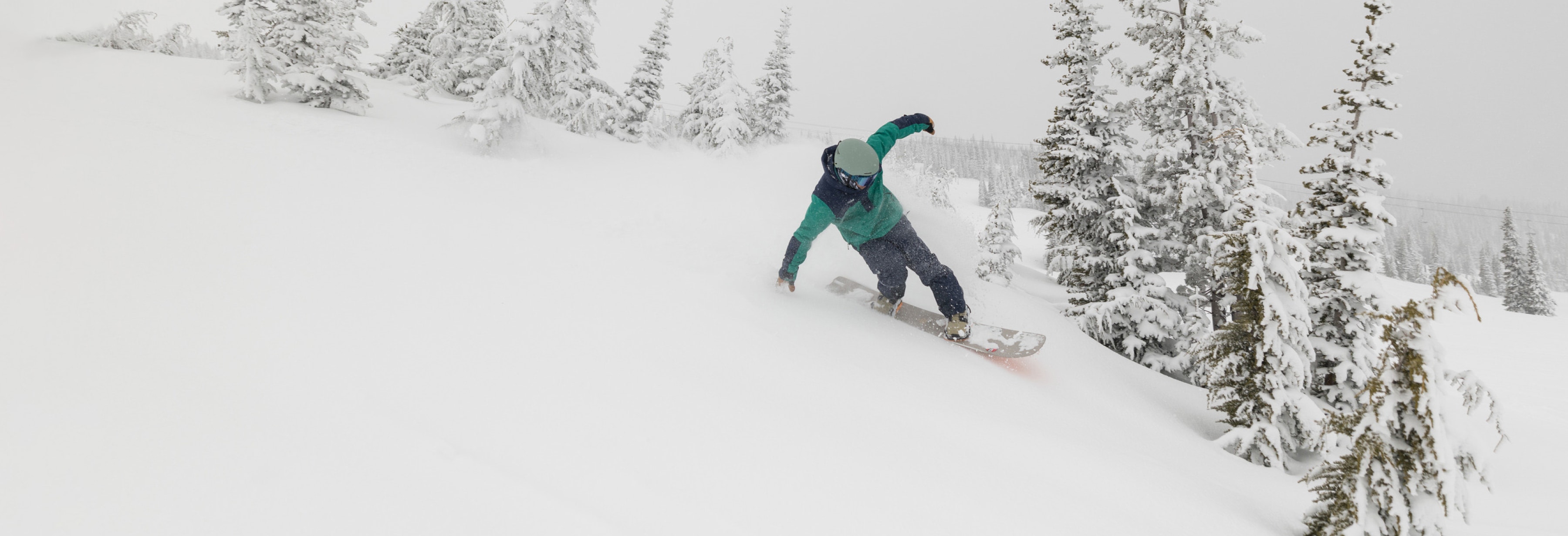 A snowboarder rides down a mountain on a snowy day.