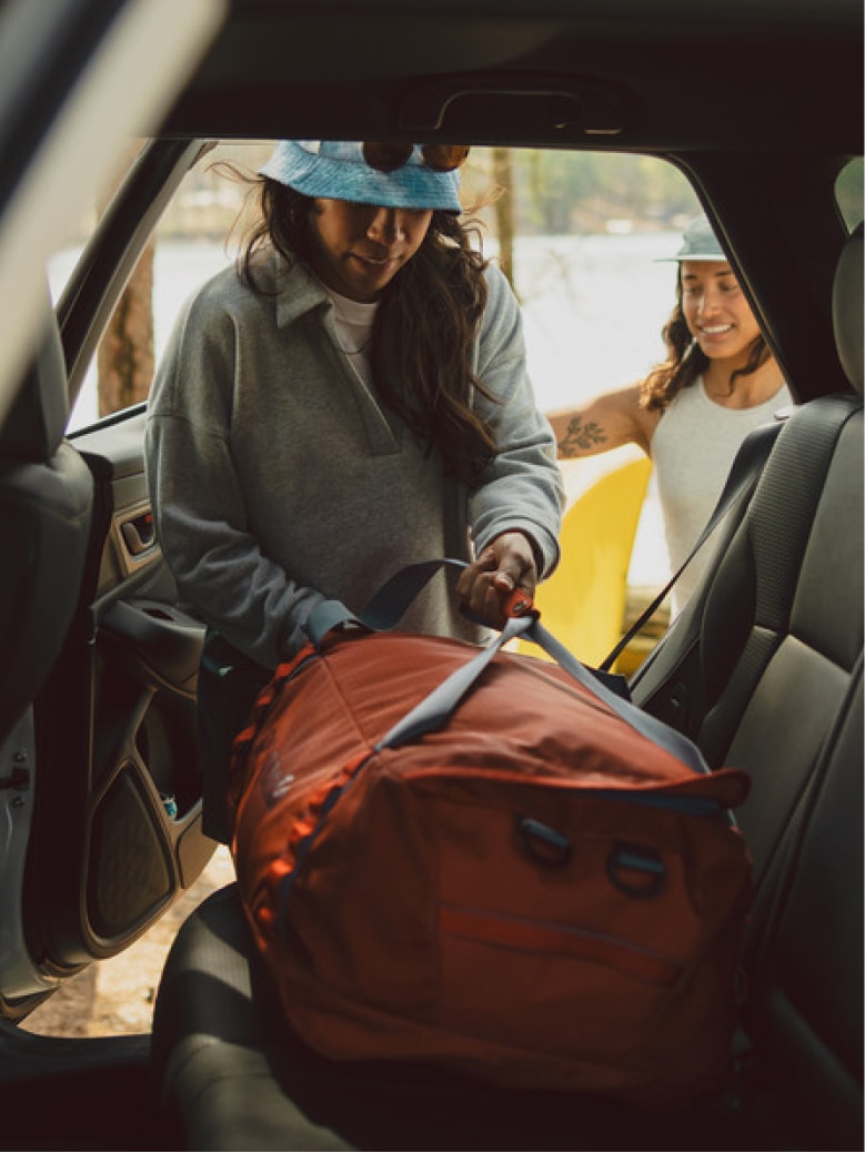 A person grabs their duffel bag from inside of a car.