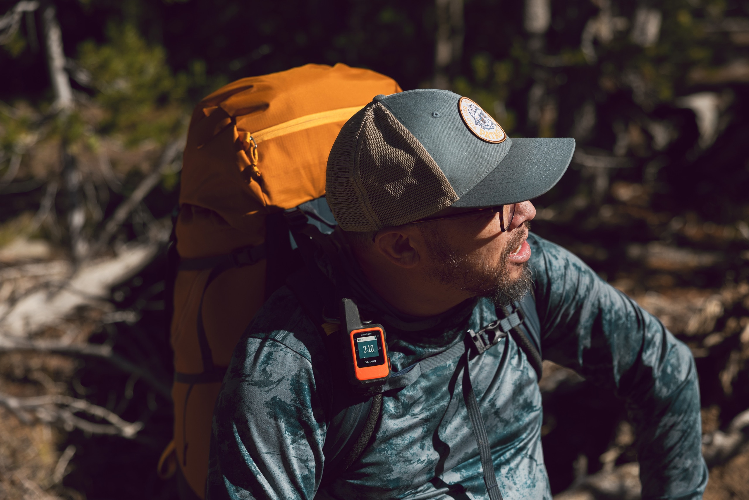 A backpacker has a satellite messenger clipped to his pack for easy reach.