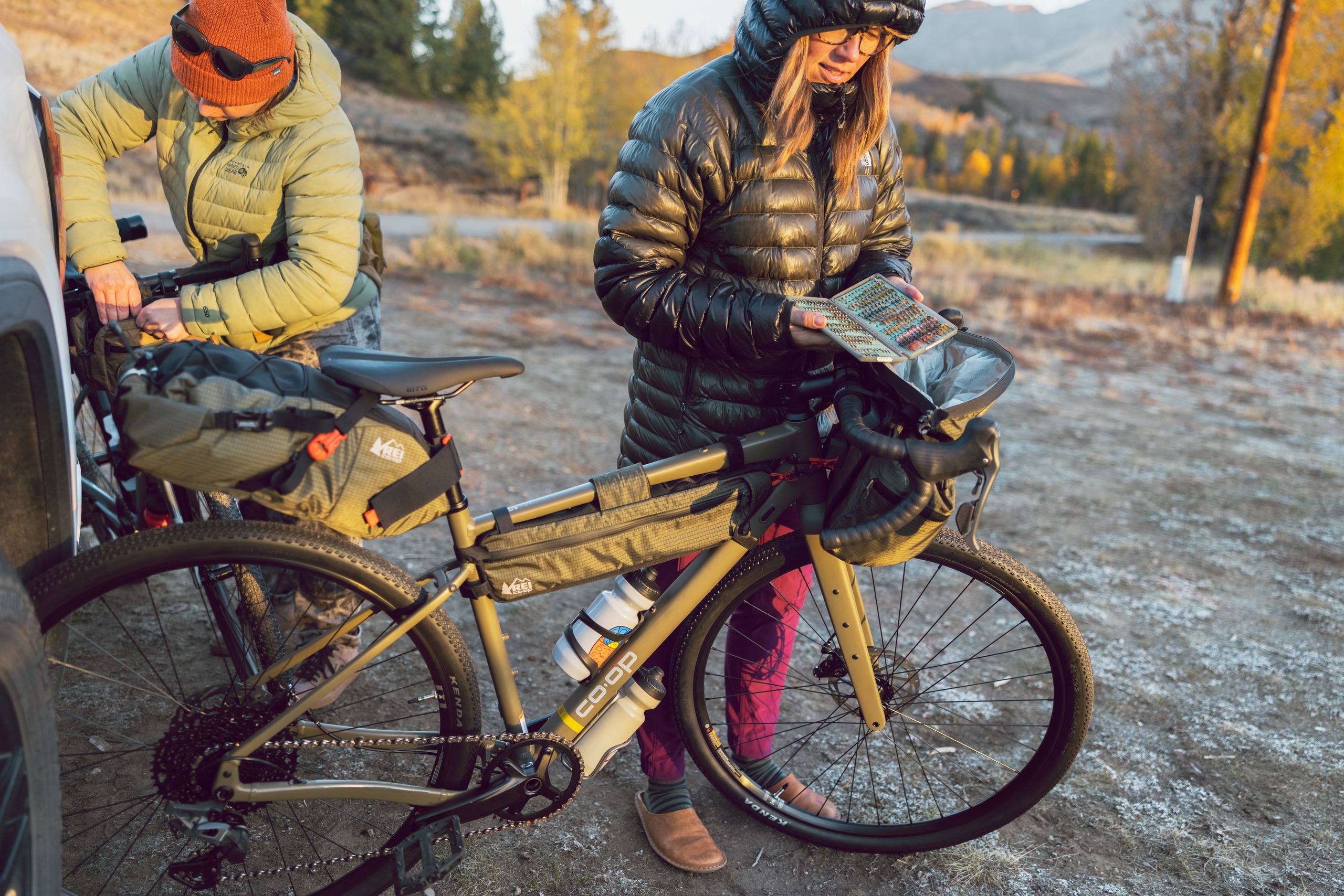 Two cyclists load up gear on a bike that has a saddle pack, frame bag and handlebar bag.