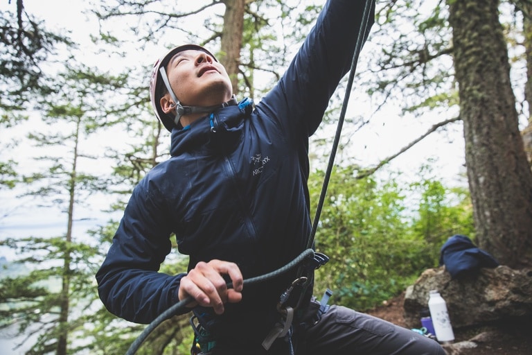 A person wears a puffy jacket while belaying another climber.