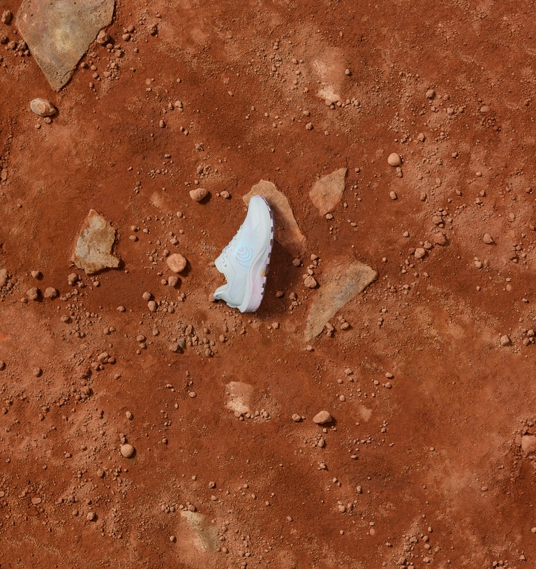 A single, light blue Topo Athletic MTN Racer 4 trail-running shoe lying on a clay-red dirt path