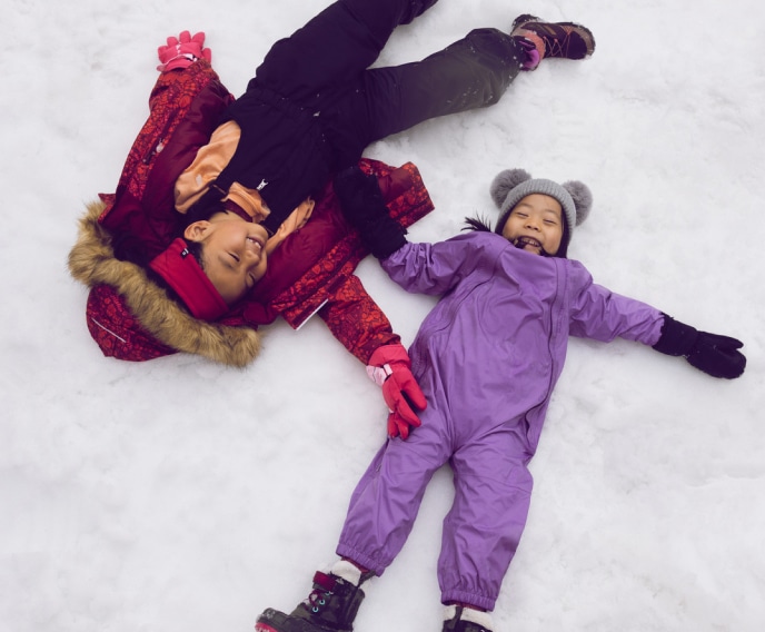 Two kids lay in the snow while laughing.