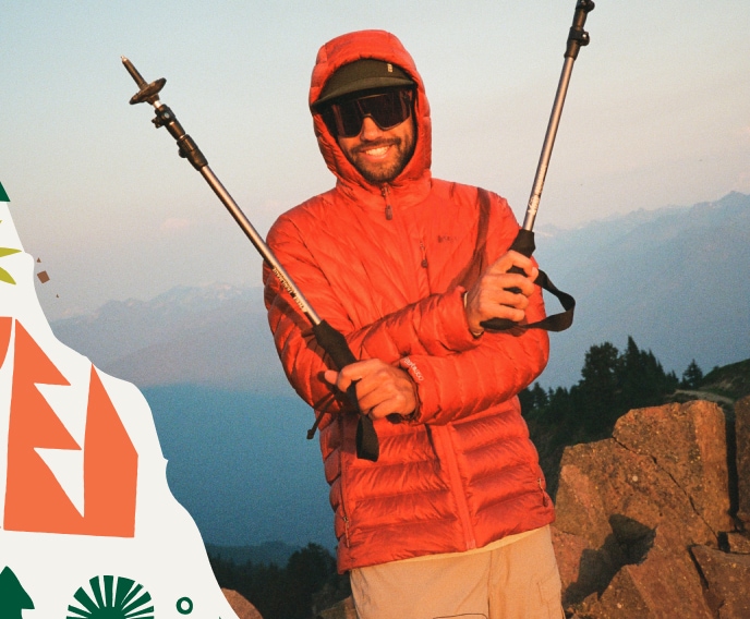 A person smiles for the camera while holding their trekking poles up.