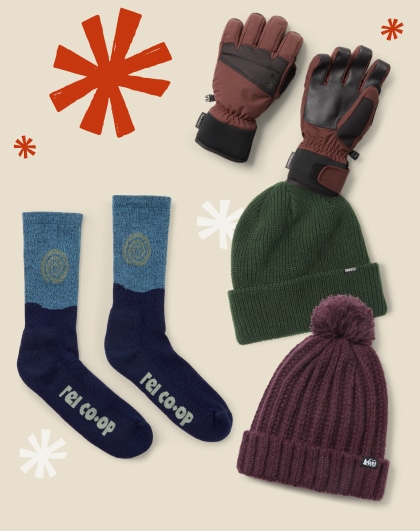 Two beanies, a pair of socks, and gloves on a light colored background with snowflakes.