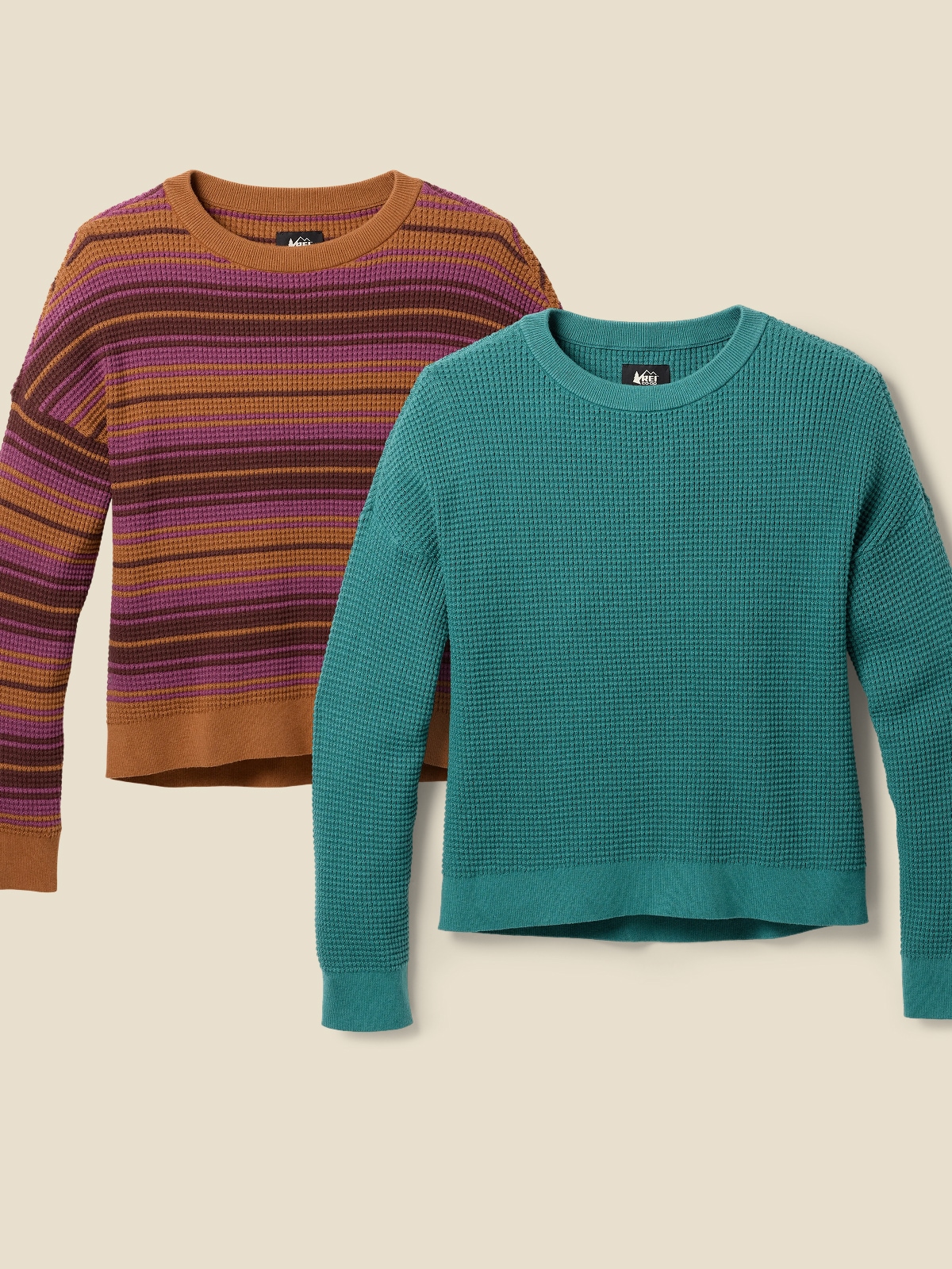 Two R E I Co-op brand sweaters on a light colored background.