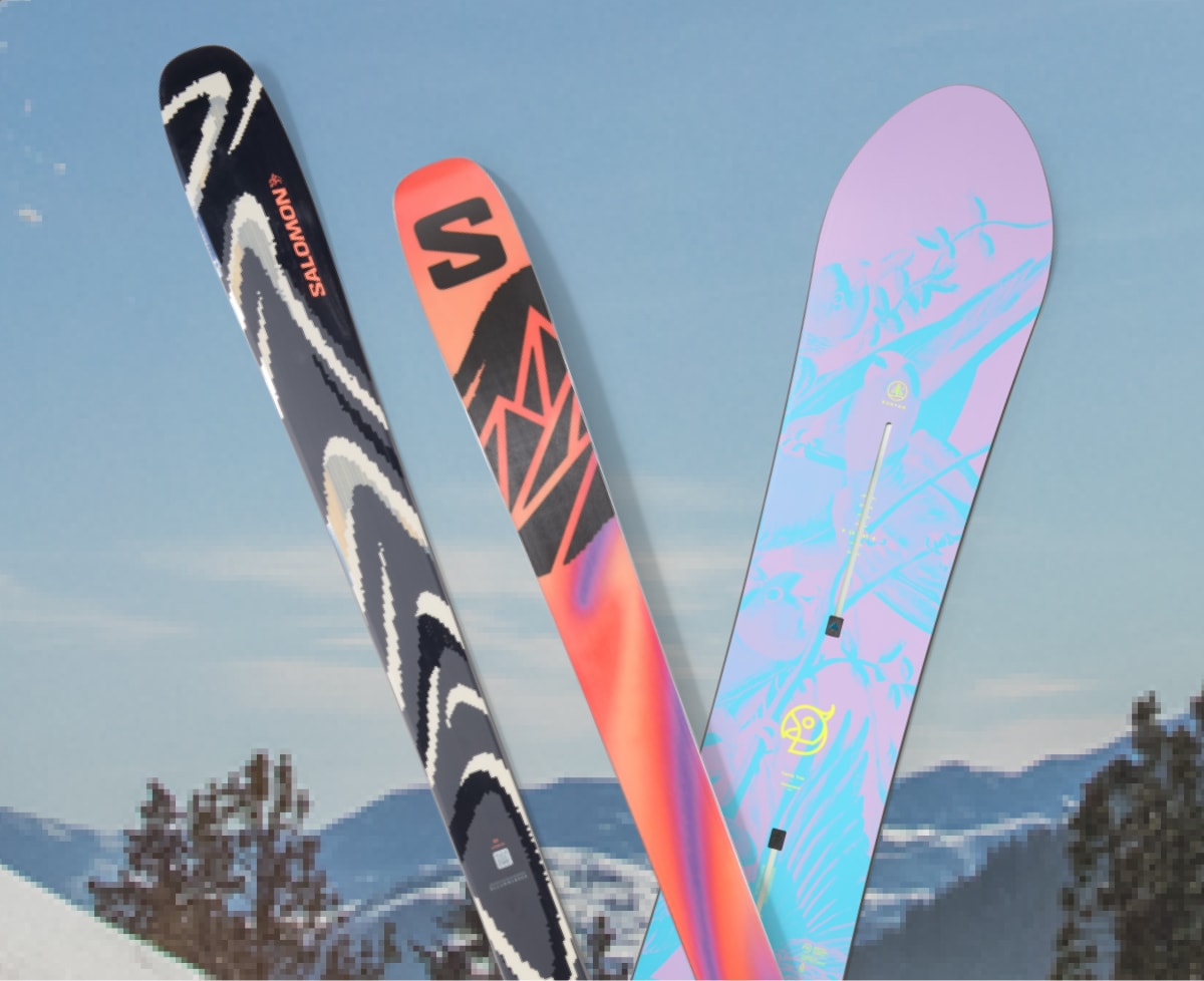 A colorful snowboard and a pair of skis with snowy mountains in the background.