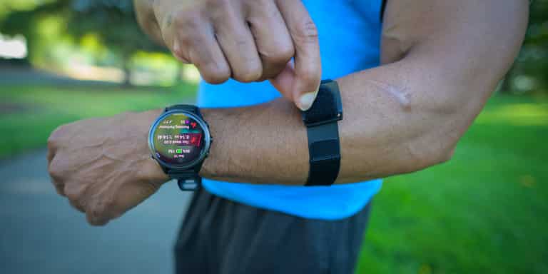 A runner adjusting an armband heart rate monitor above their wrist-only heart rate monitor/watch;