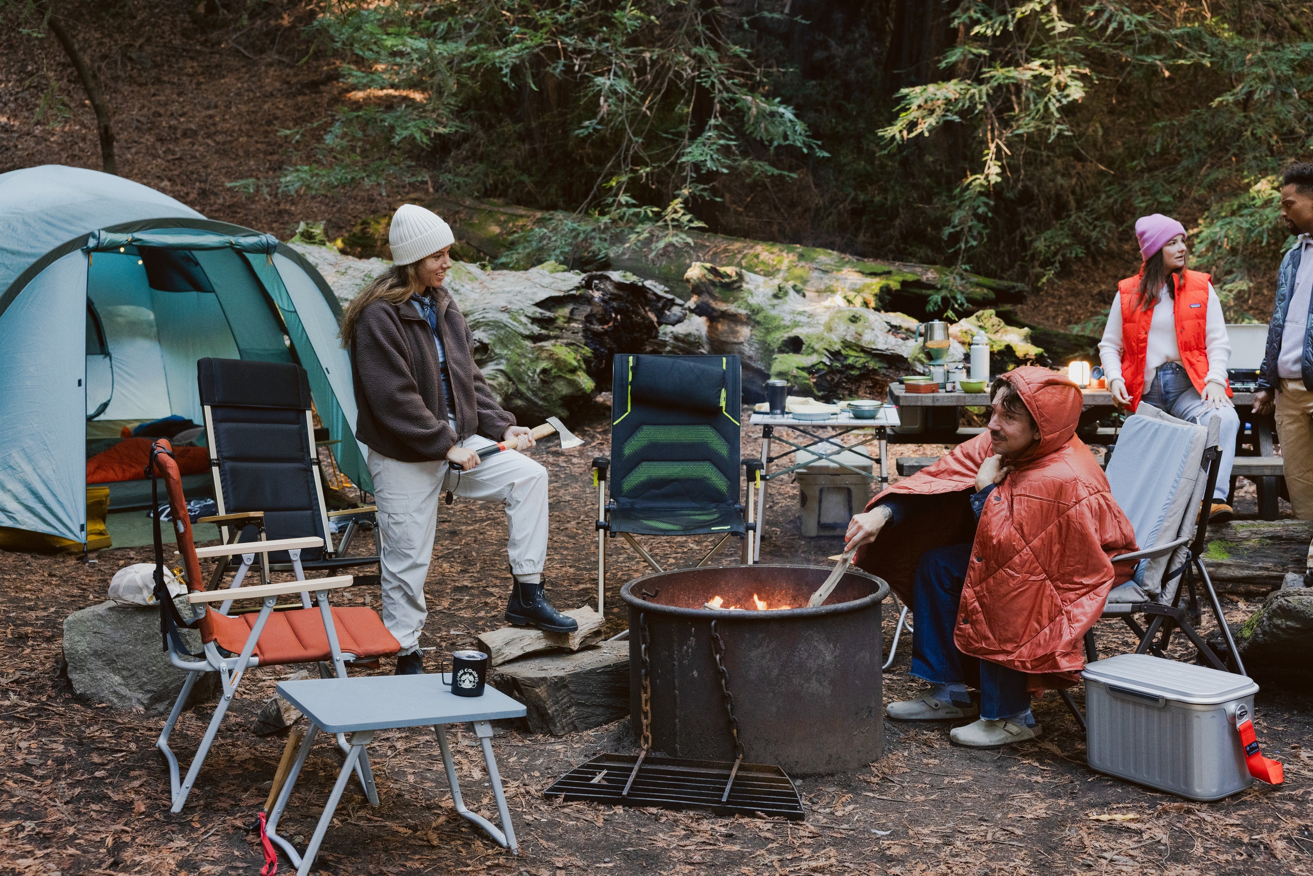 Several campers are gathered around a campfire with lots of camp chairs for seating