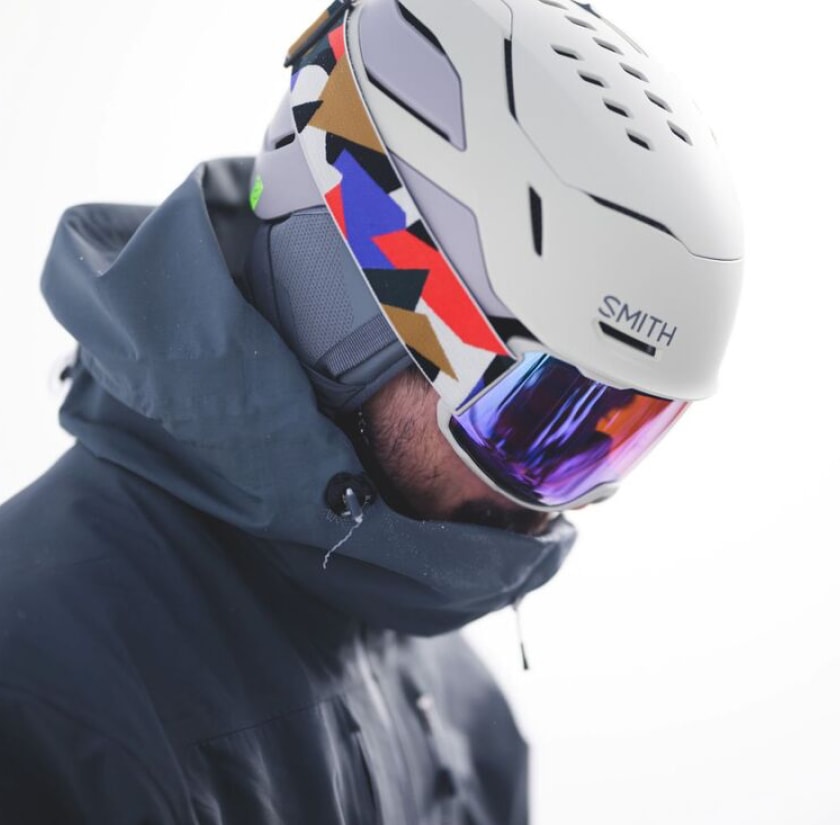 A person looks down while wearing a Smith snow helmet and colorful goggles.