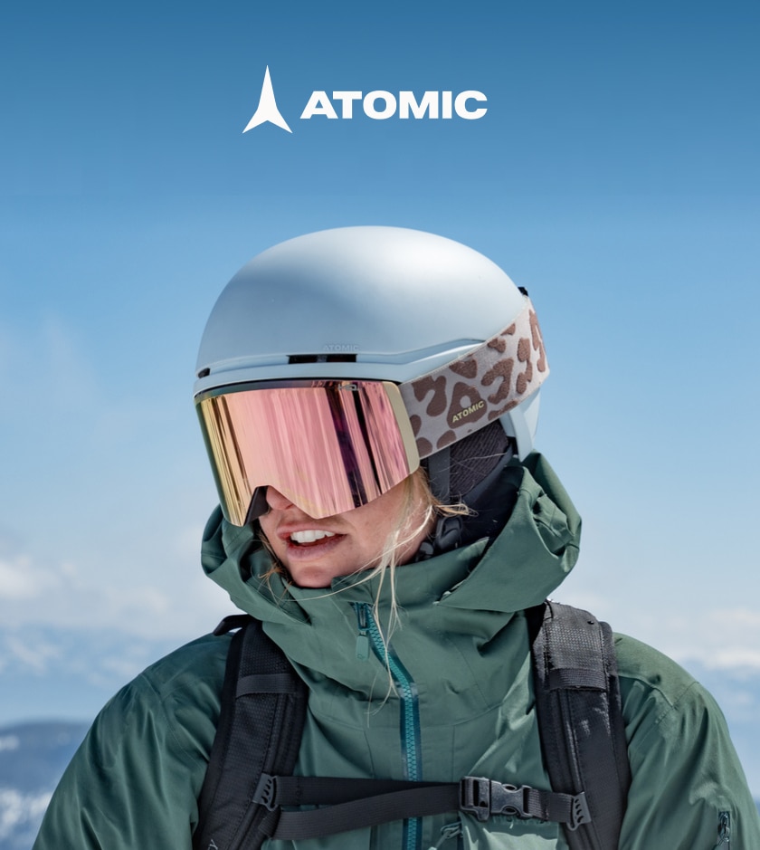 A person bundled up in snow gear looks off to the side while wearing an Atomic snow helmet and goggles.