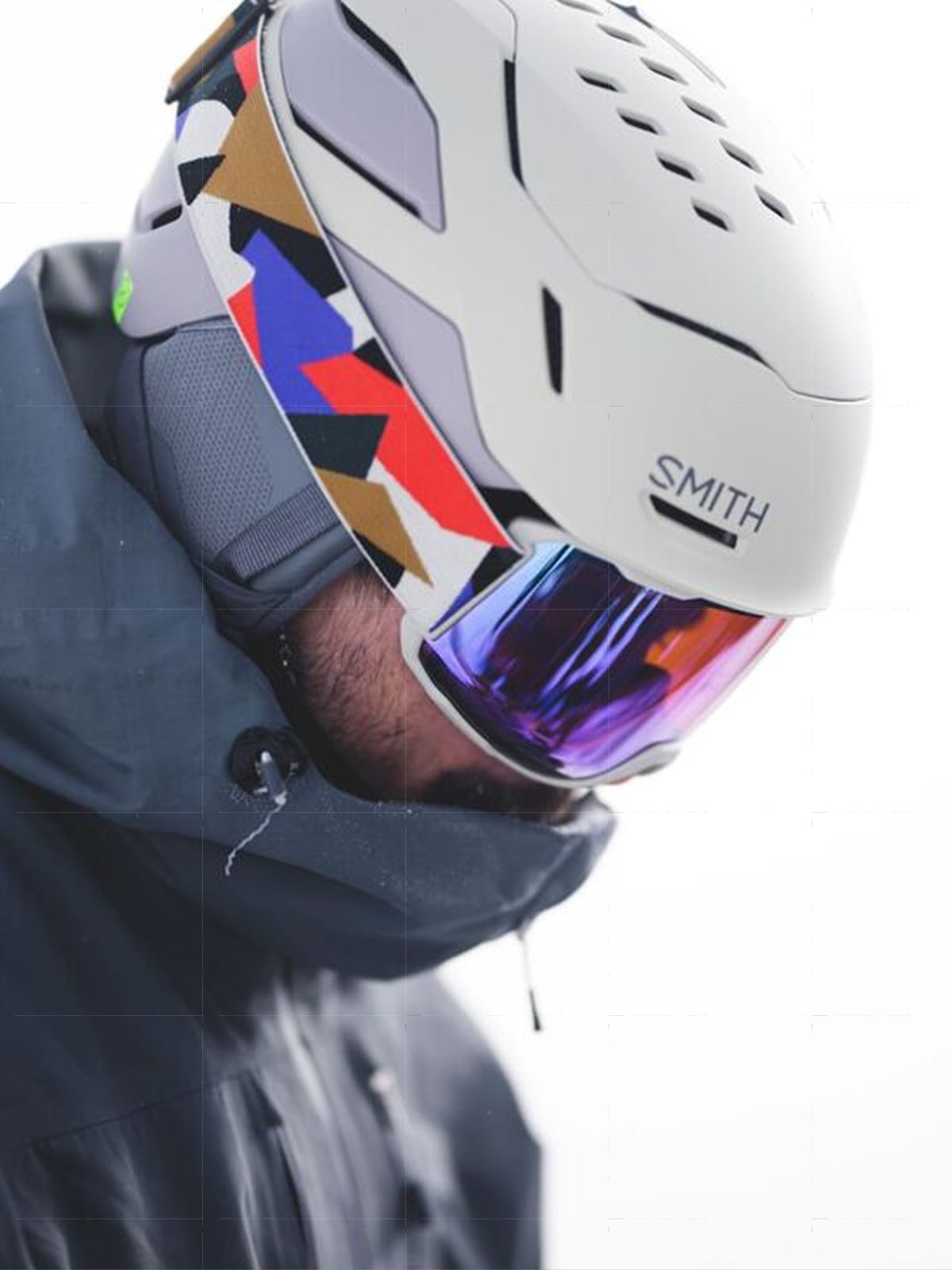 A person looks down while wearing a Smith snow helmet and colorful goggles.
