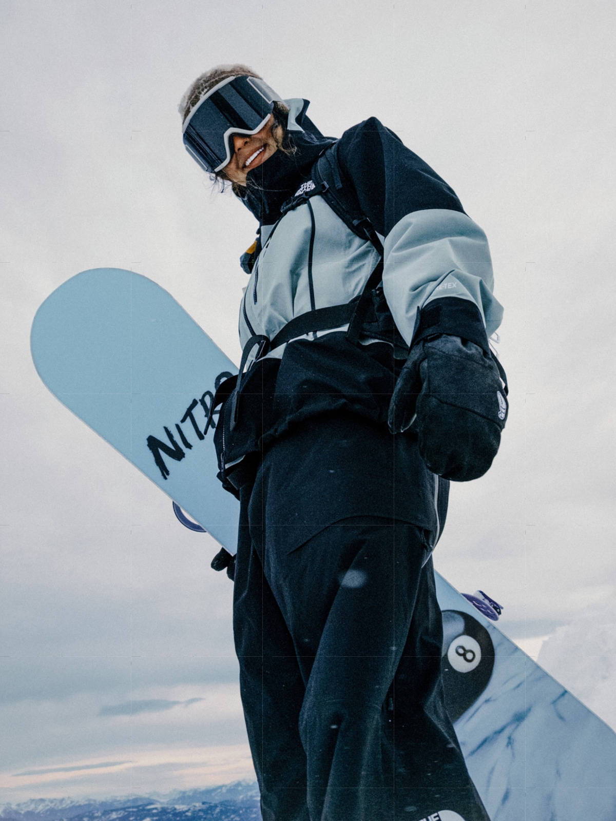 A person wearing The North Face snow gear holds a snowboard and smiles for the camera.