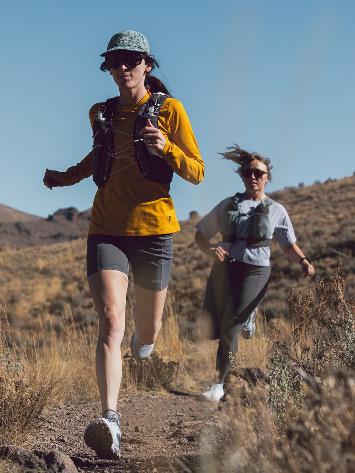 Two people run through a dirt trail on a sunny day.