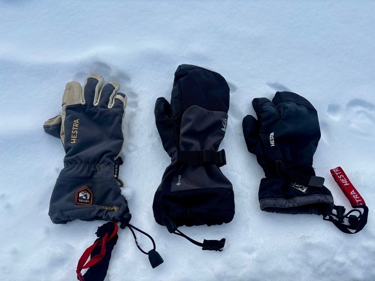 Three different gloves pictured on snow: gloves, mittens and a split-finger option.