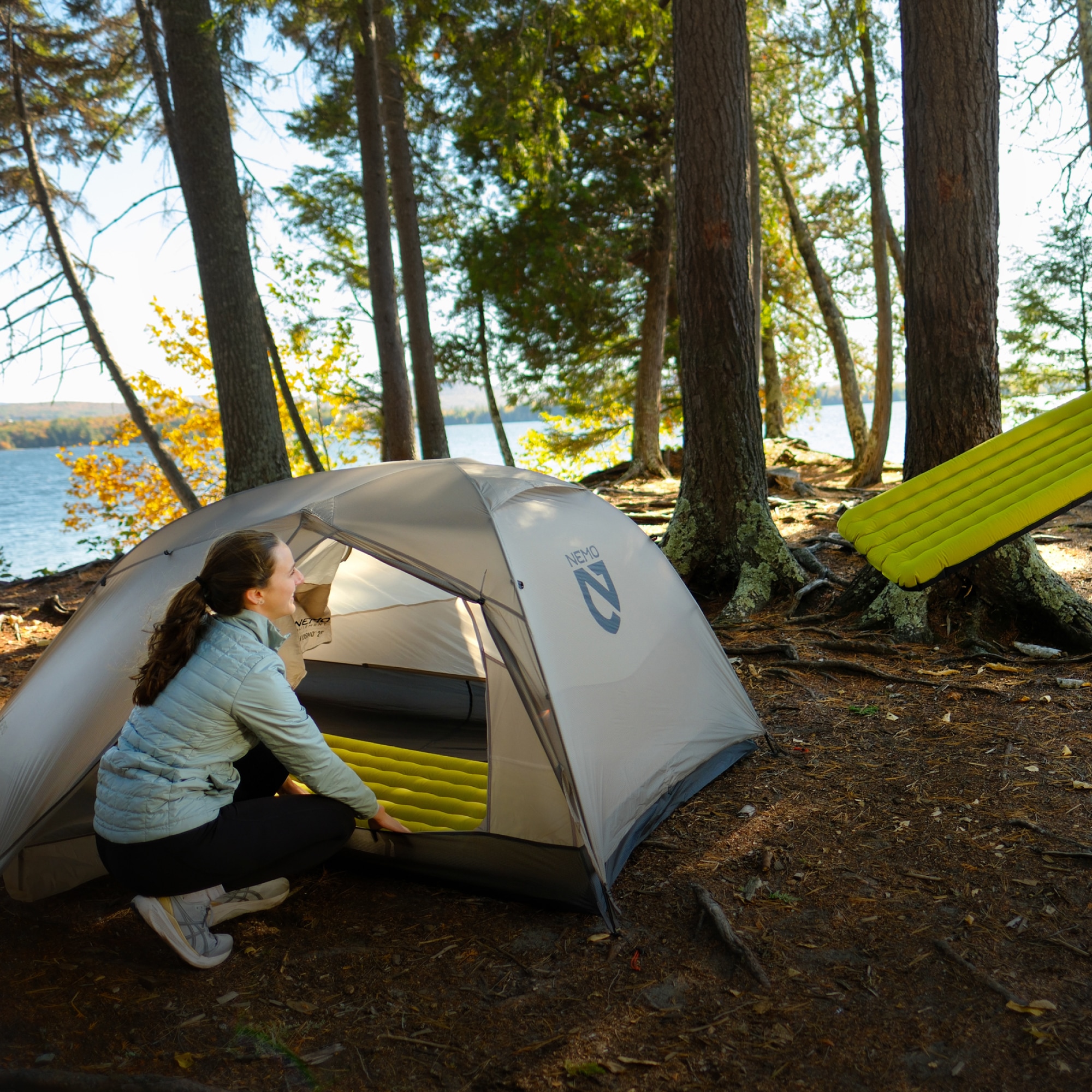 A person kneels near the opening of a NEMO tent.