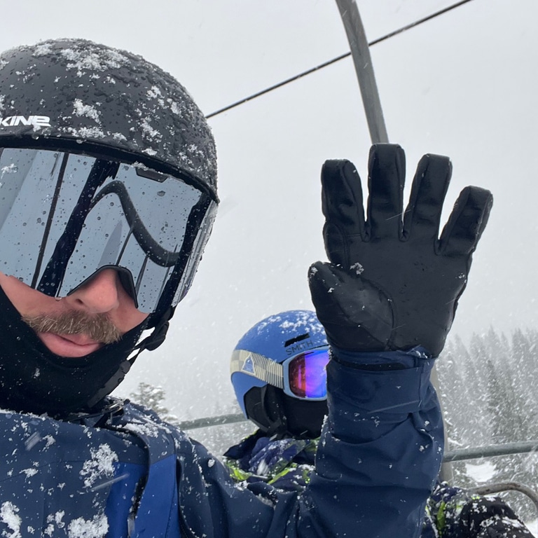 An adults waves while riding a ski chair lift with a kid