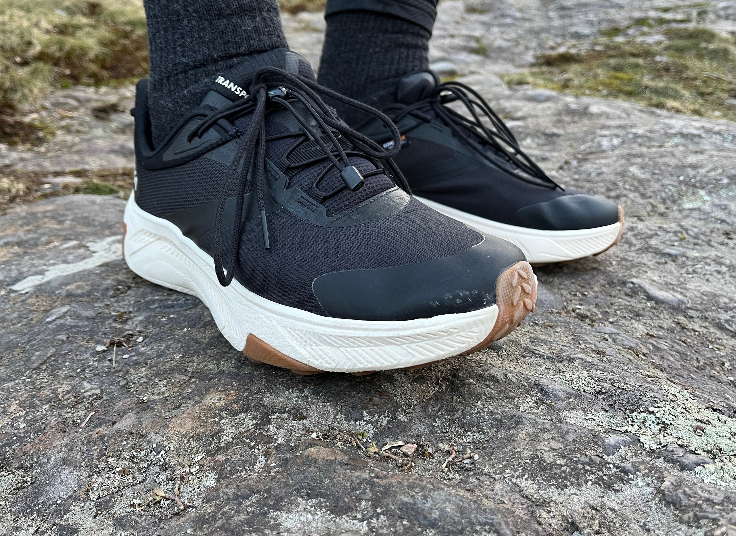 A close up on a pair of HOKA Transport 2 shoes worn on a rocky surface