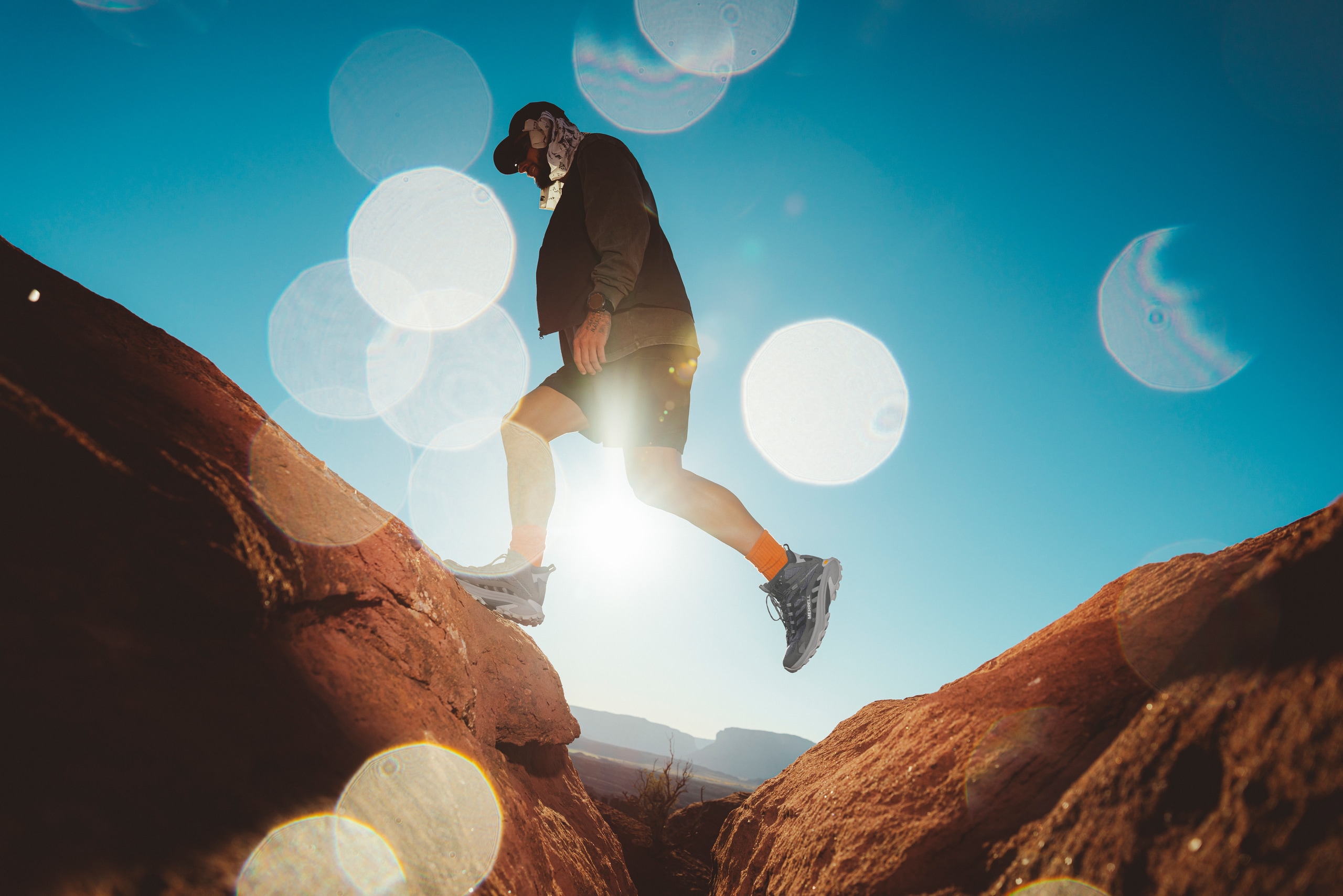 A person in hiking apparel and hiking boots steps from one large red rock to another outdoors under a dark blue sky