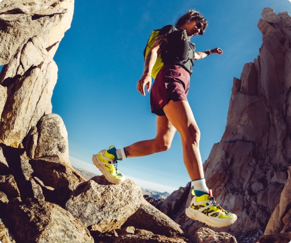 A person wearing HOKA hiking boots climbs across a rocky trail.