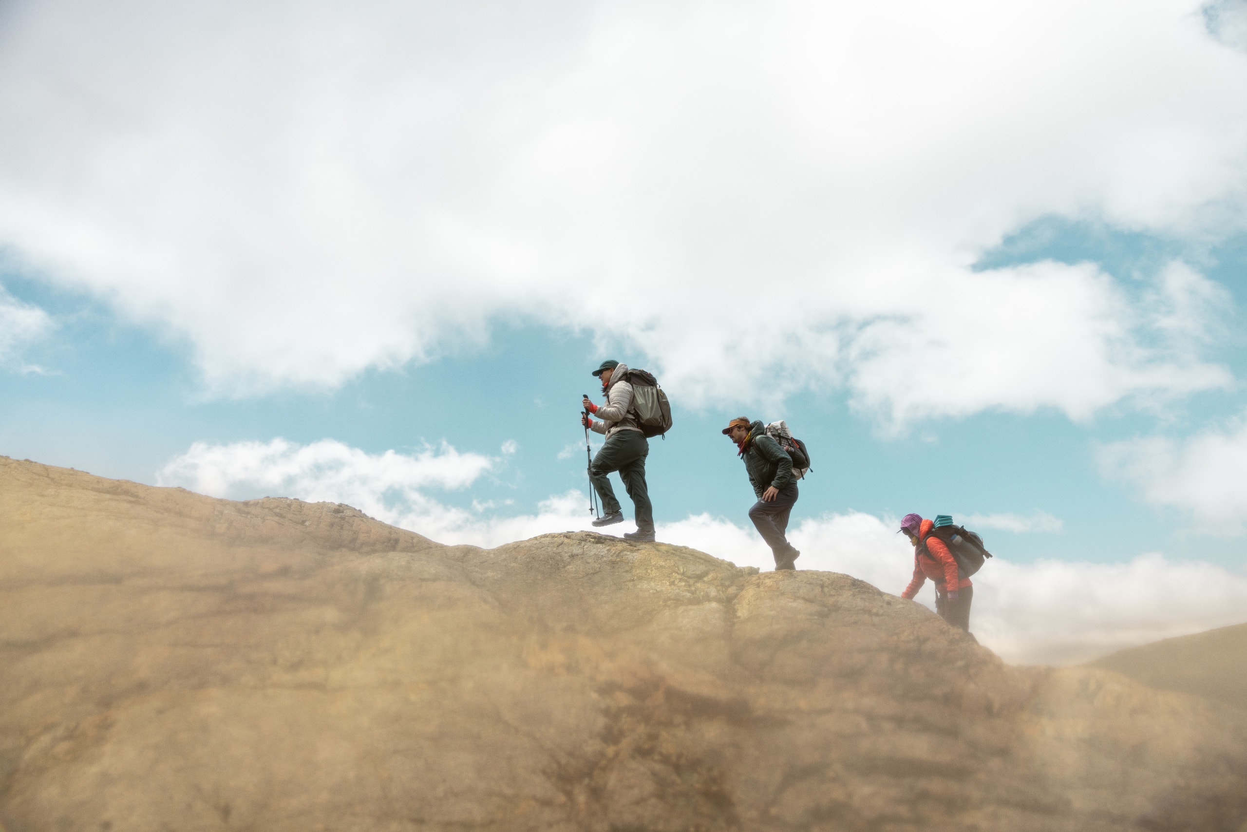 Three hikers ascend a rock face on a cloudy day.