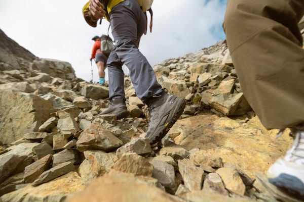 Three hikers ascend a rocky mountain path.
