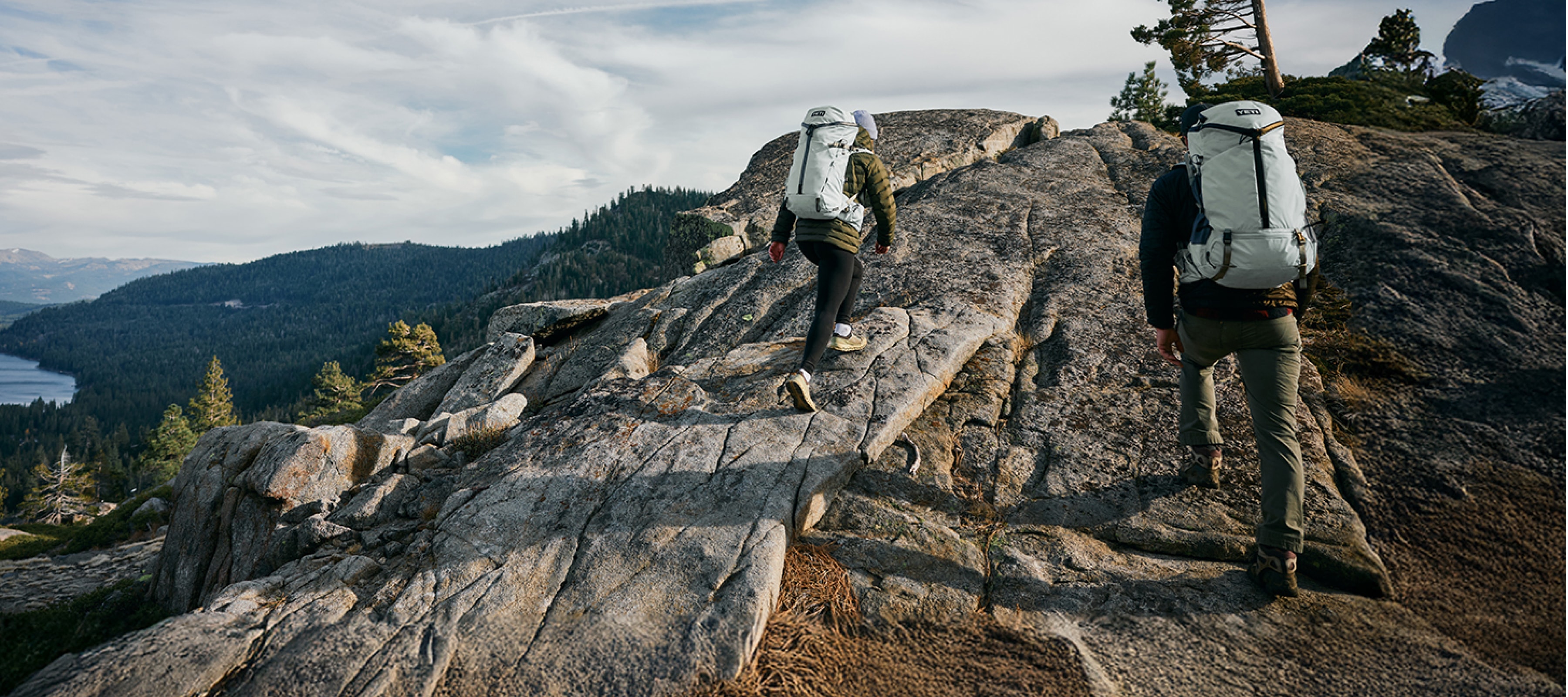 Two people hike up a rocky hill with matching YETI backpacks on.