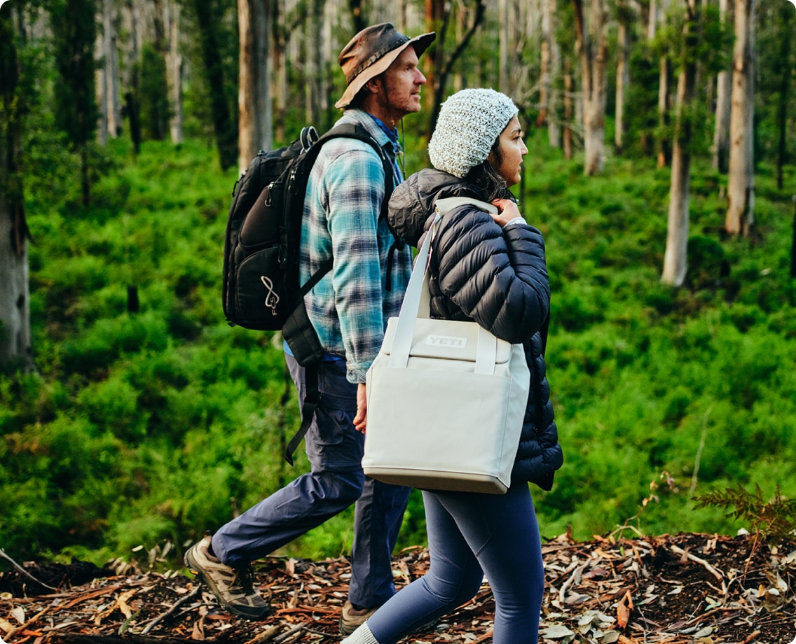 Two people walk through a forest with a YETI Daytrip lunch bag.