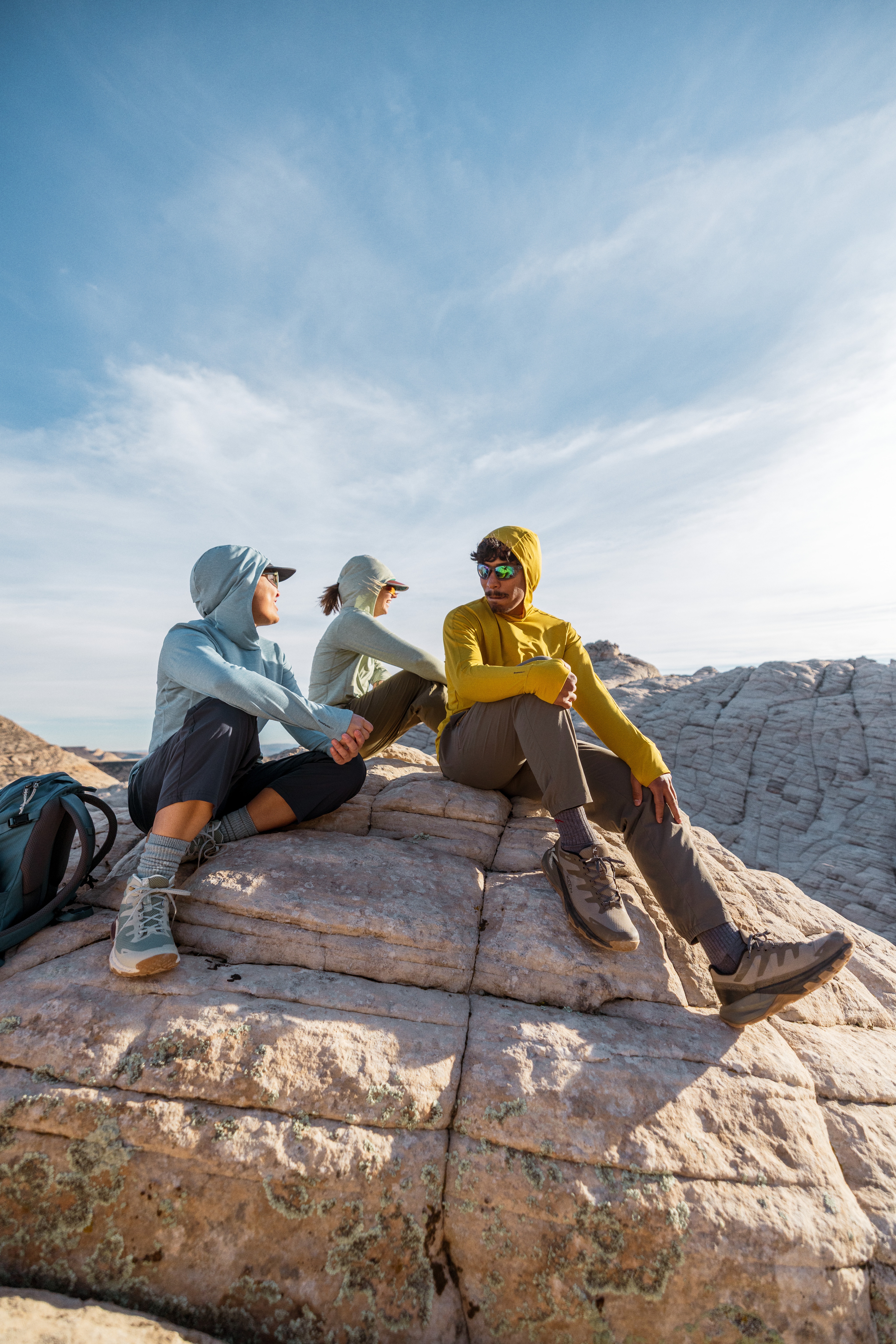 Three people sitting on a rock at the top of a hill.