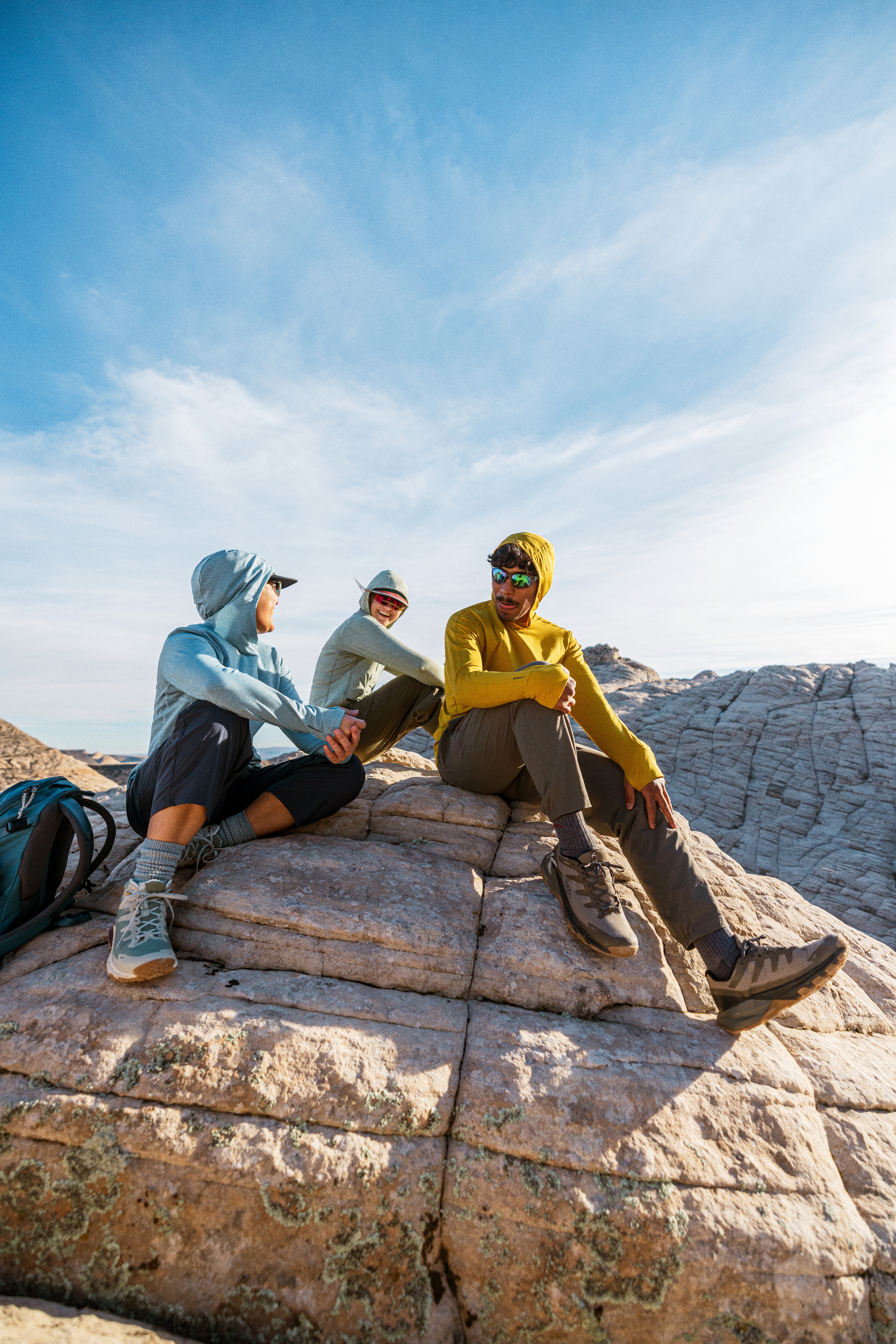 Three hikers sit on a large rock in their Sahara Shade Hoodies.