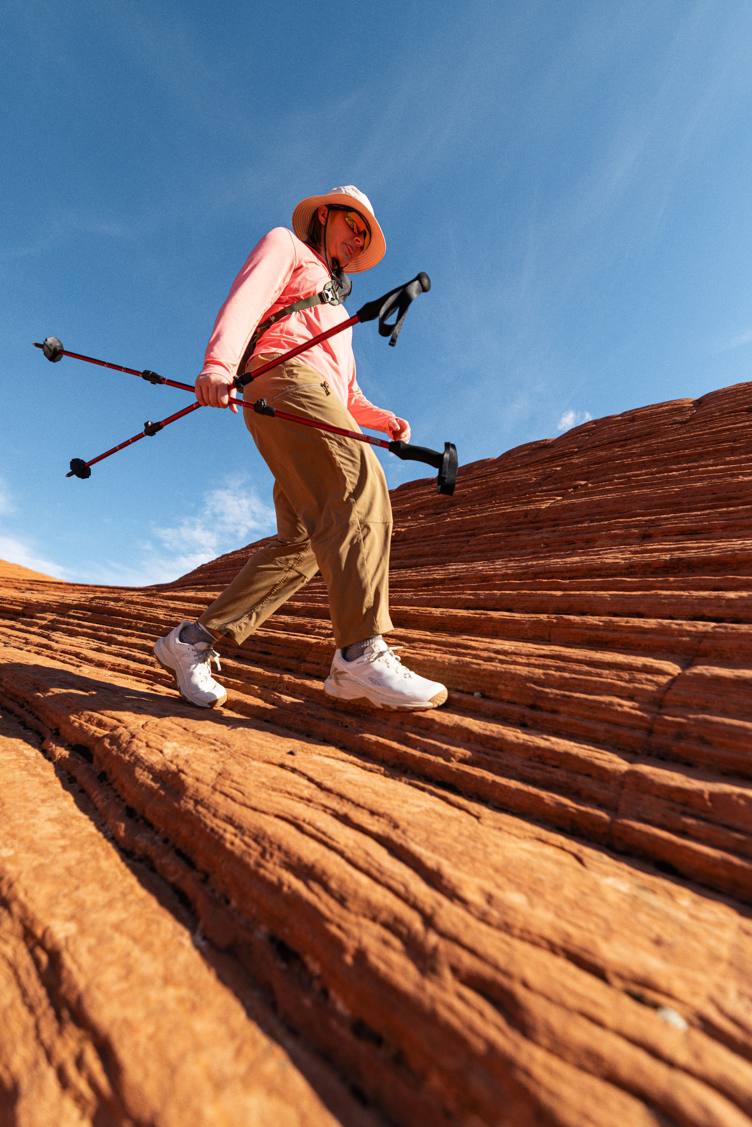 A person steps across red rocks while holding two trekking poles.
