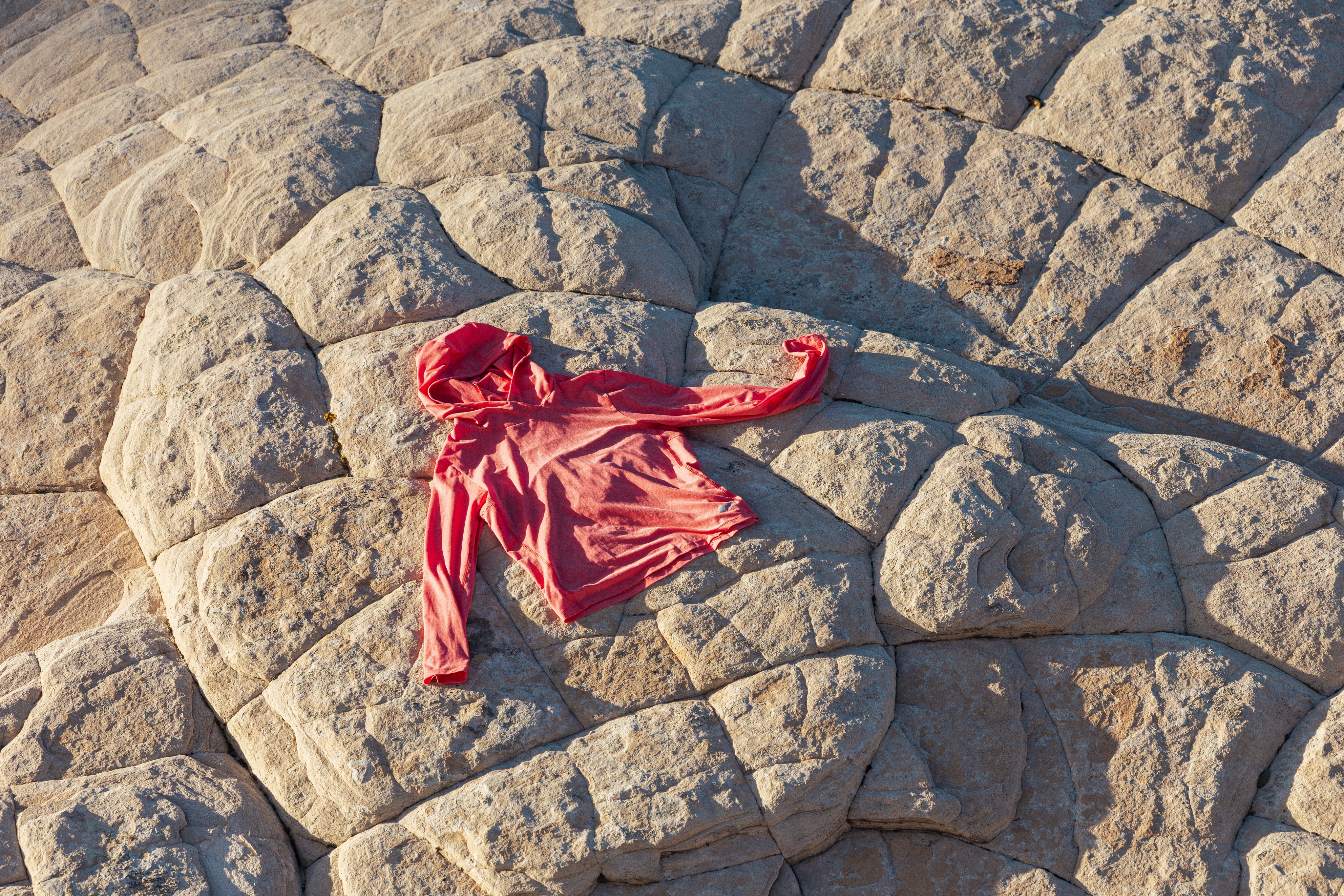A red REI Co-op brand sun hoodie laying on top of a large rock formation.